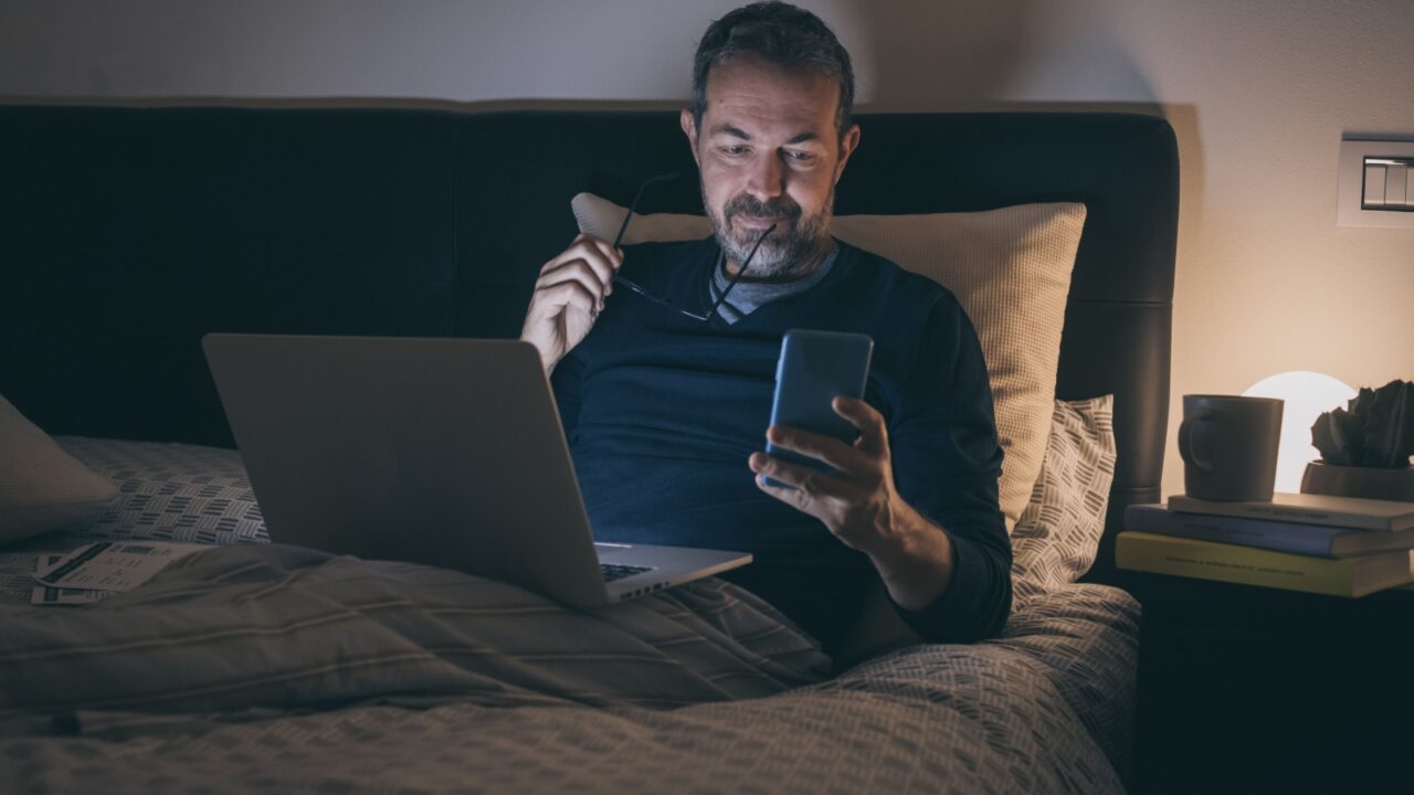 Man works with laptop lying on bed. Male home working with remote office. Boy sitting in bedroom use online devices. Smart working, home school, internet lifestyle new communication technology concept