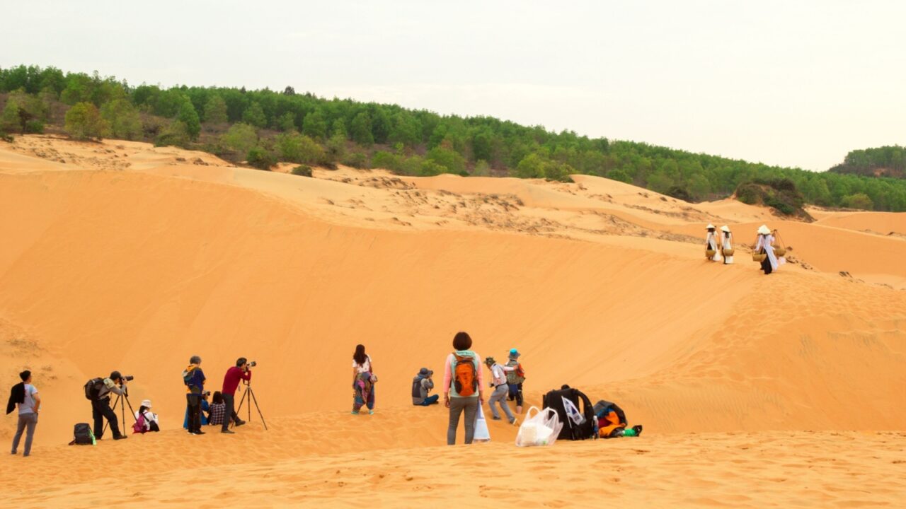 Mui Ne, Vietnam - March 21, 2018: Group of tourists taking photos in sand dunes of desert landscape