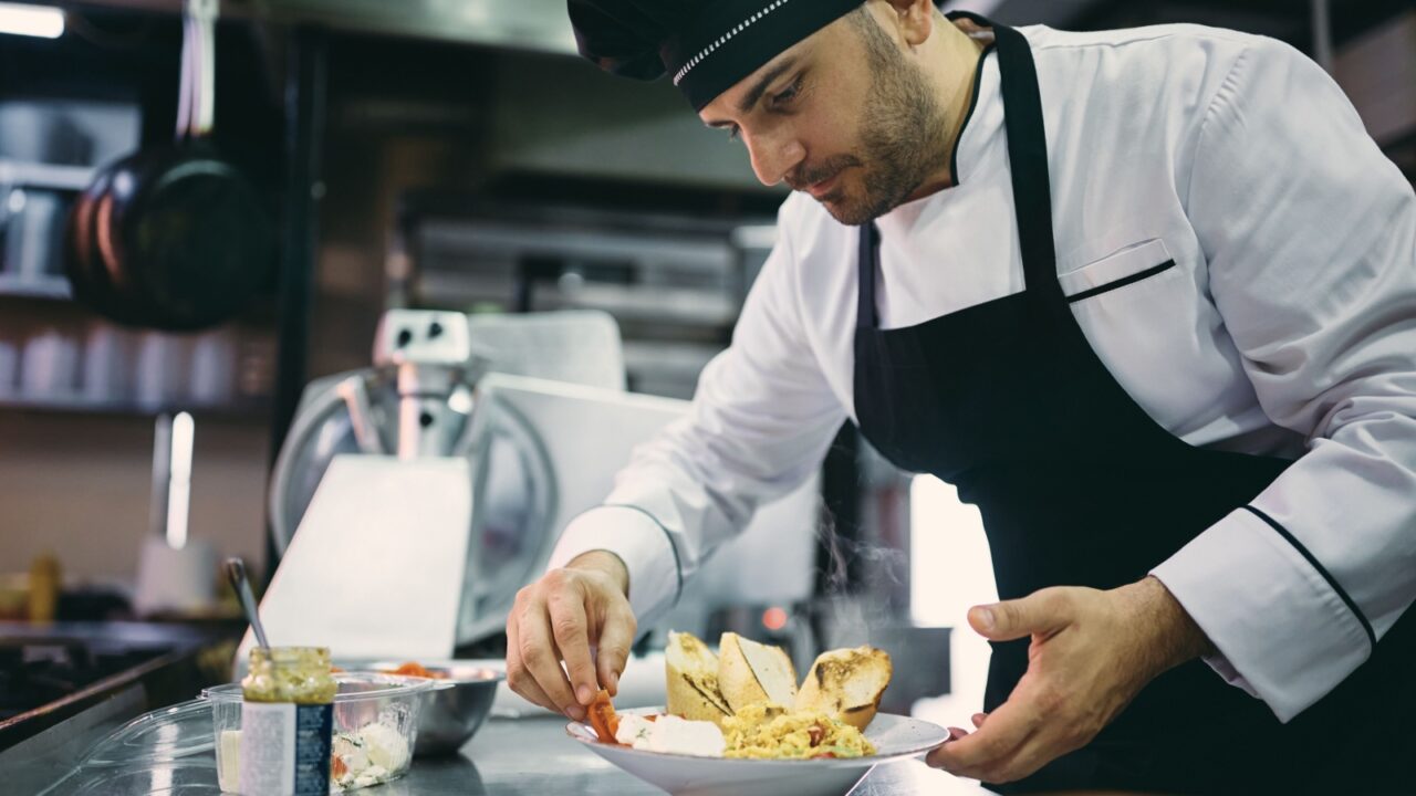 Professional cook serving a meal while working in the kitchen at restaurant.