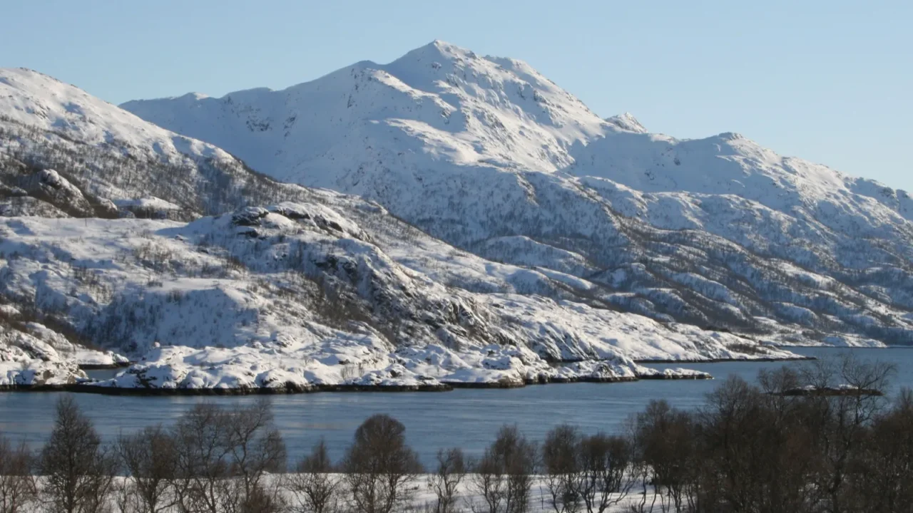 a mountain near the river is covered with snow in