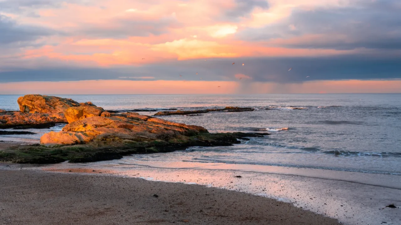 beautiful winter sunset over a sandy beach with sunlit rocks