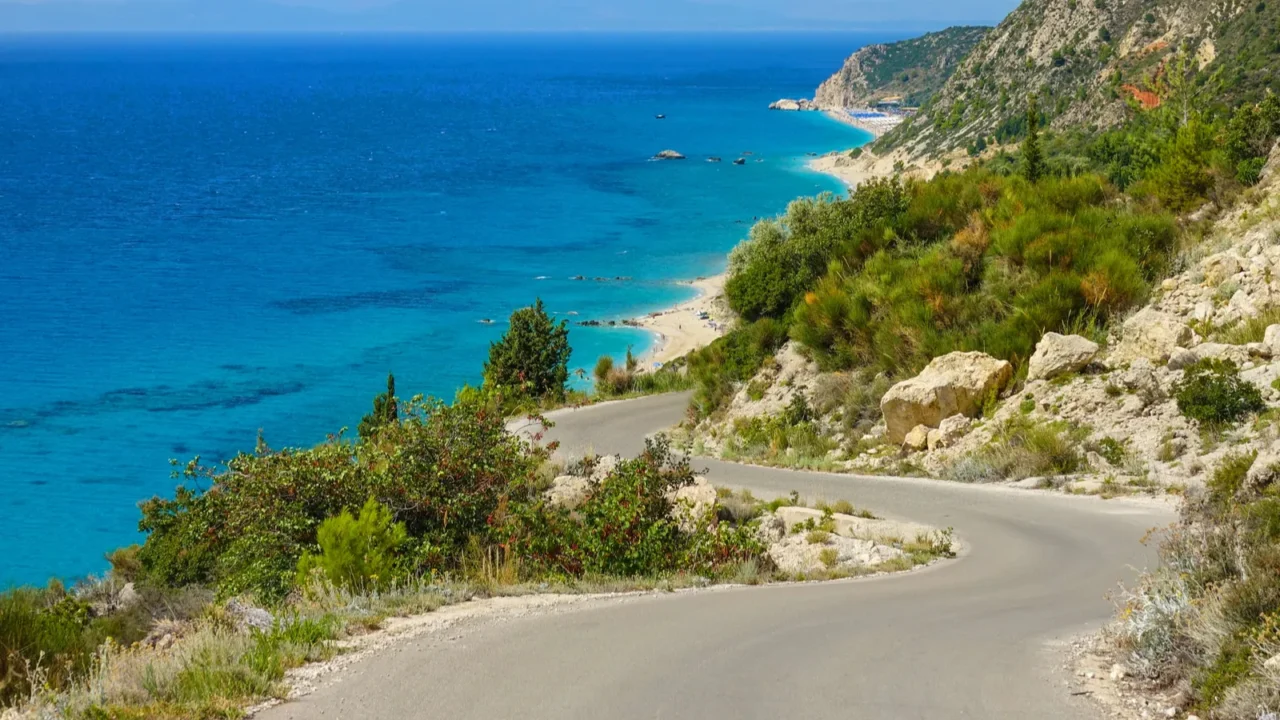 empty asphalt road winds along rugged mediterranean terrain and turquoise