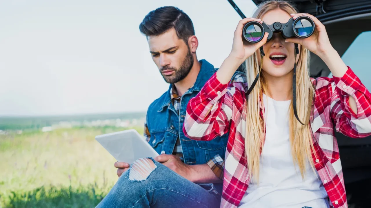 female tourist looking through binoculars while her boyfriend using digital