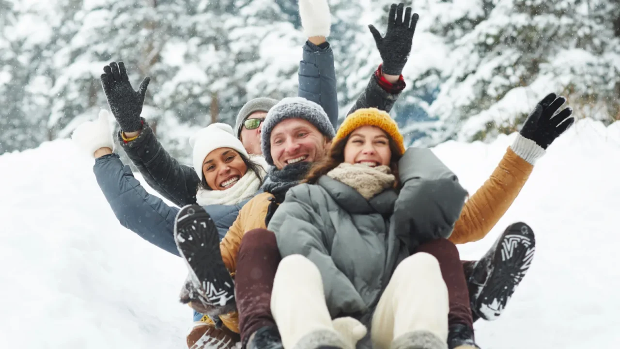 four funny friends in winterwear riding down hill in snow