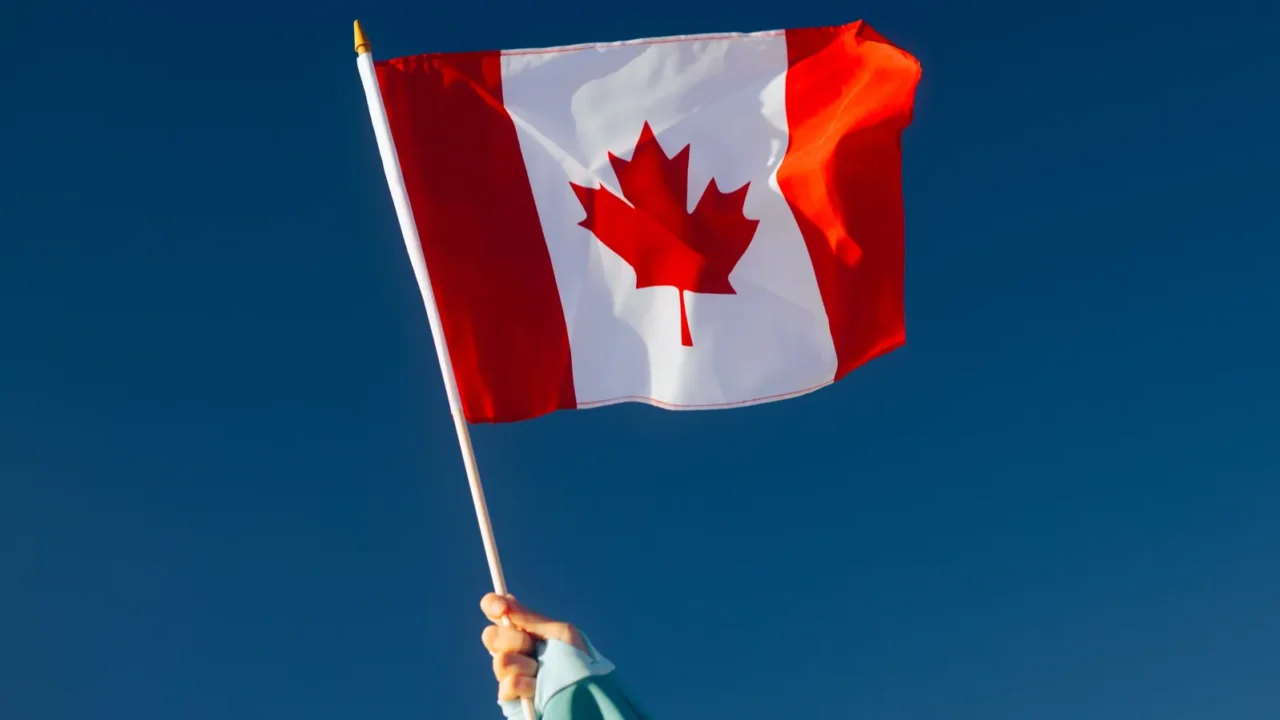 hand waiving a canadian flag on a blue sky