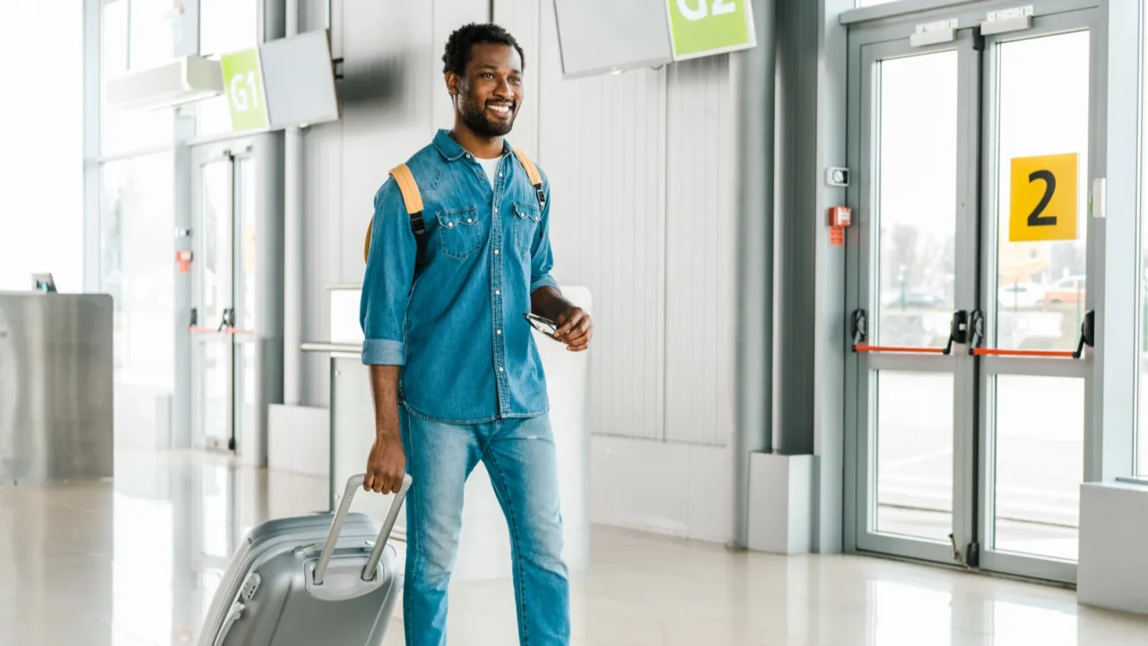 happy handsome african american man walking with suitcase in airport