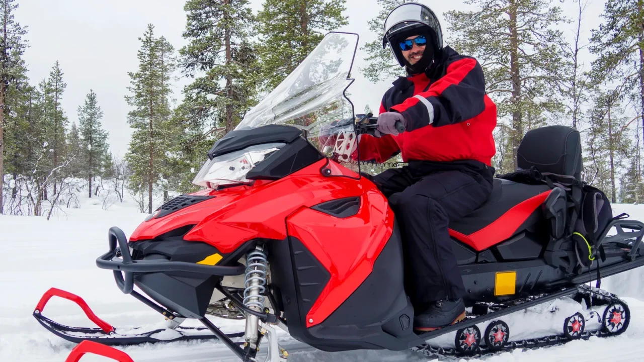 happy smiling man driving snowmobile in finnish lapland