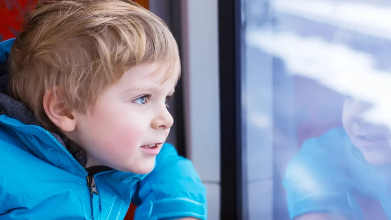 little kid boy traveling and looking out train window outside