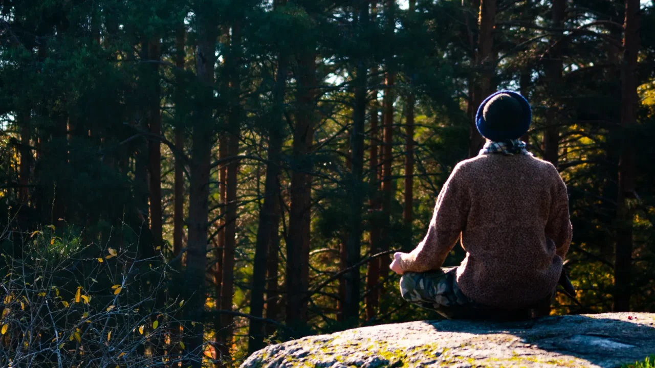 man in a sweater meditates on a rock