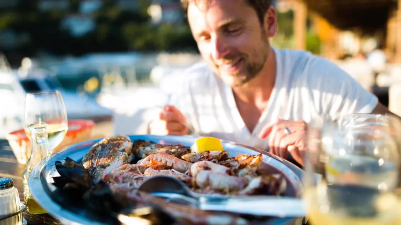 man on holiday sitting outside at sunset eating seafood