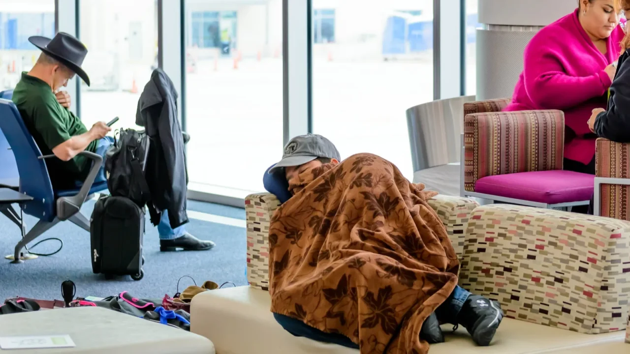 man sleeping in an airport under a blanket