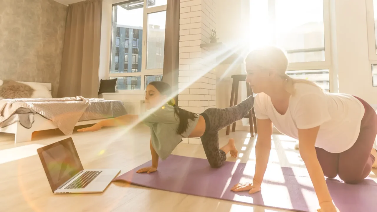 mother and daughter make yoga exercise online with laptop at