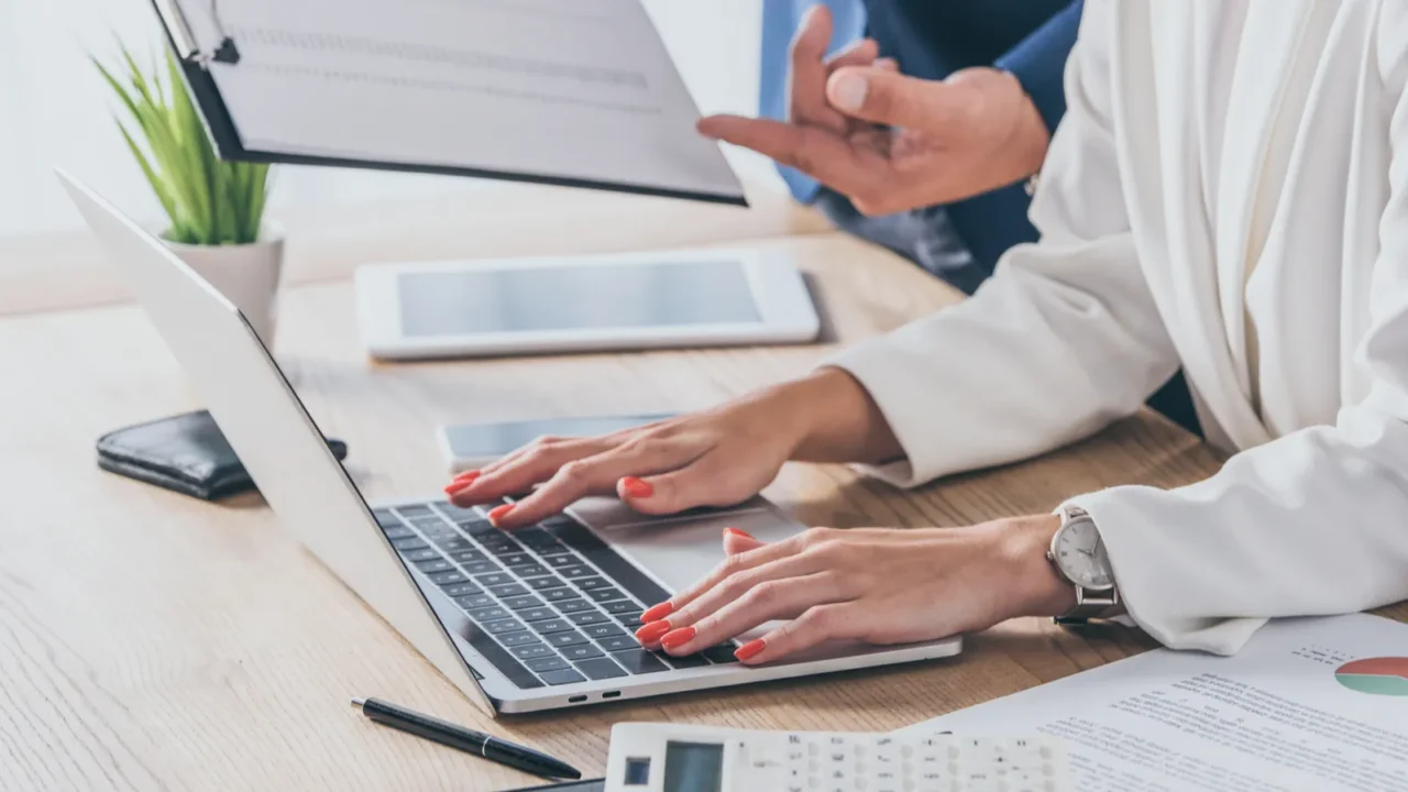 partial view of businessman holding clipboard near businesswoman using laptop