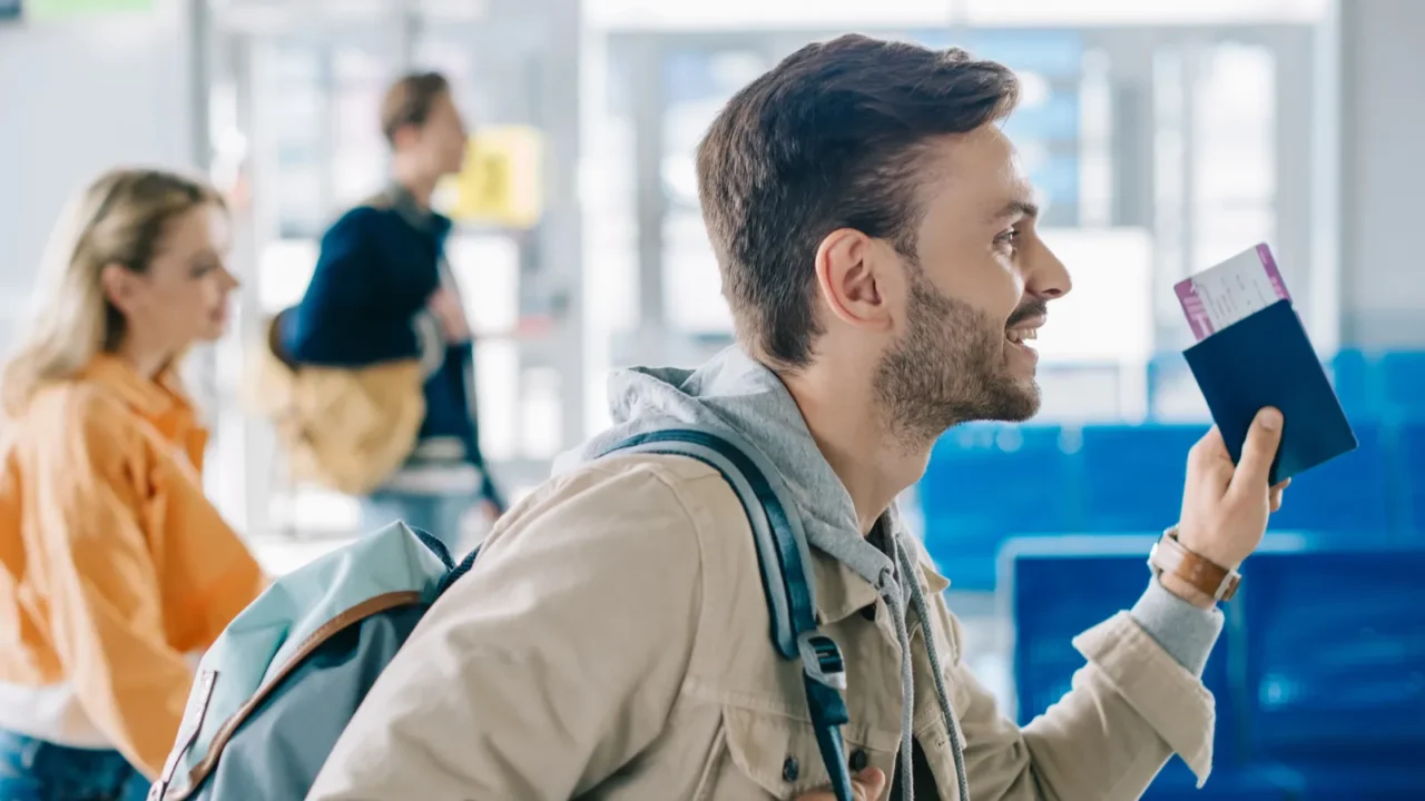 side view of smiling man with backpack holding passport and