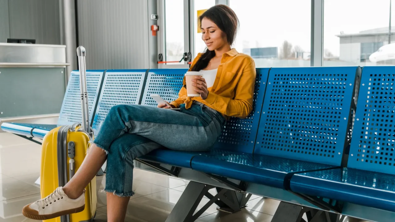 smiling african american woman sitting in departure lounge with suitcase