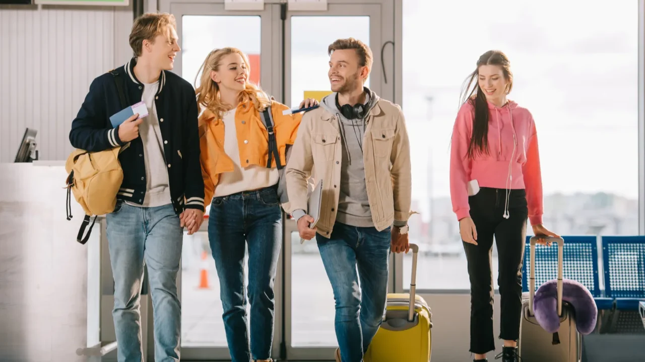smiling young friends with documents and luggage in airport terminal