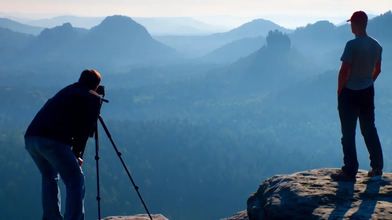 tourist guide and photo enthusiast stay with tripod on cliff