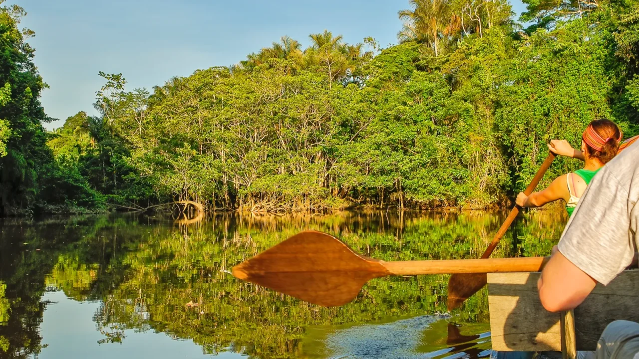 two people rowing a canoe with paddles in calm waters
