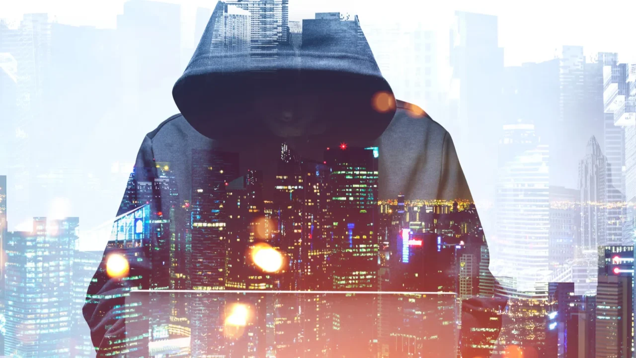 unrecognizable young hacker in hoodie using laptop in blurry city