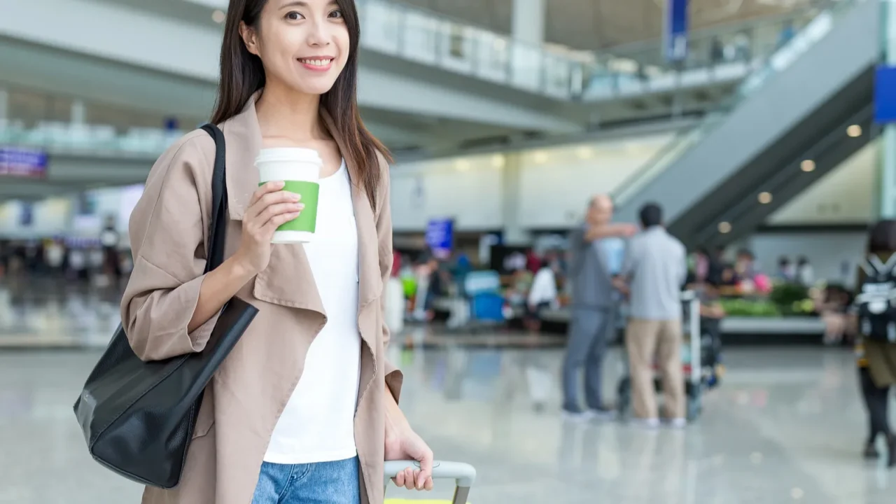 woman holding luggage and coffee in airport