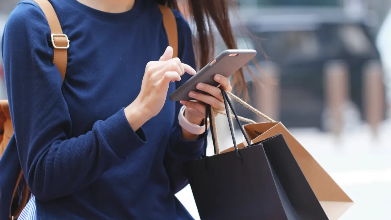 woman look at mobile phone and holding shopping bags