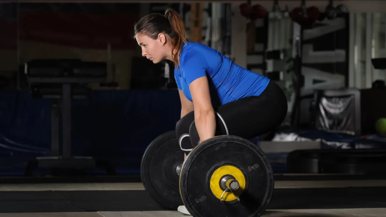 young woman doing deadlift workout with heavy barbell in dark