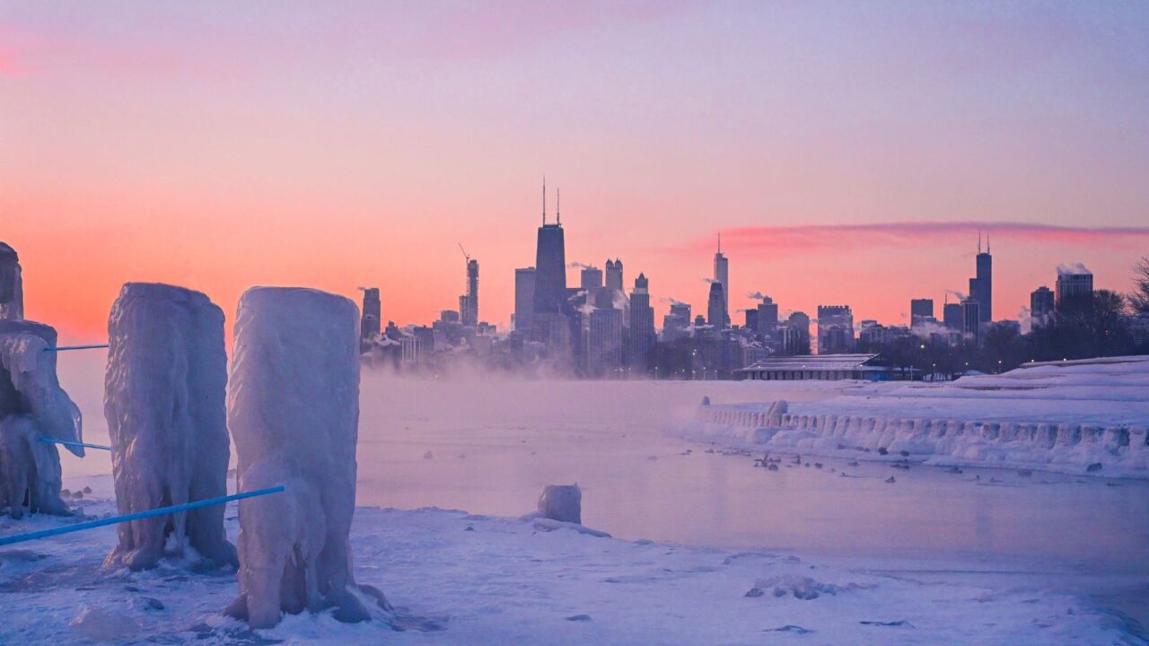The polar vortex storms over the Chicago skyline. Mist carries off a frozen Lake Michigan during a colorful sunrise.