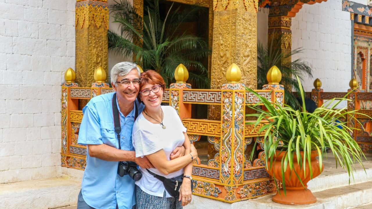 Smiling happy couple standing near the entrance of a temple at Thimphu, Bhutan. Caucasian tourists posing to the camera near the stairs of a monastery.