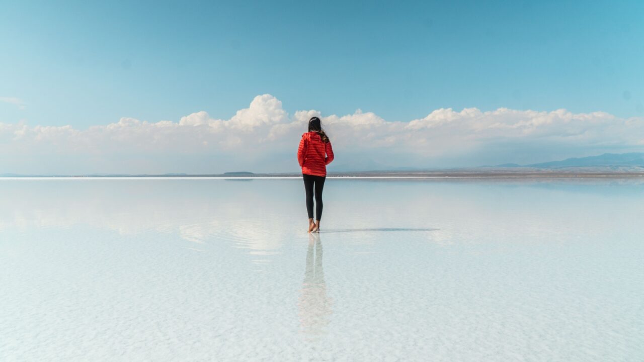 Woman tourist & beautiful mirror reflection on blue sky and cloud on Bolivia's Salt Flats. Shot in Salar de Uyuni salt flat. Water reflection of clouds and empty space. Holiday, vacation travel scene
