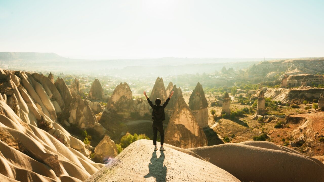 Female person stand with hands up over dramatic valley on hazy sunrise with fairy chimneys background. Solo exploration in Turkey. Cinematic Travel destination-Cappadocia 2020.