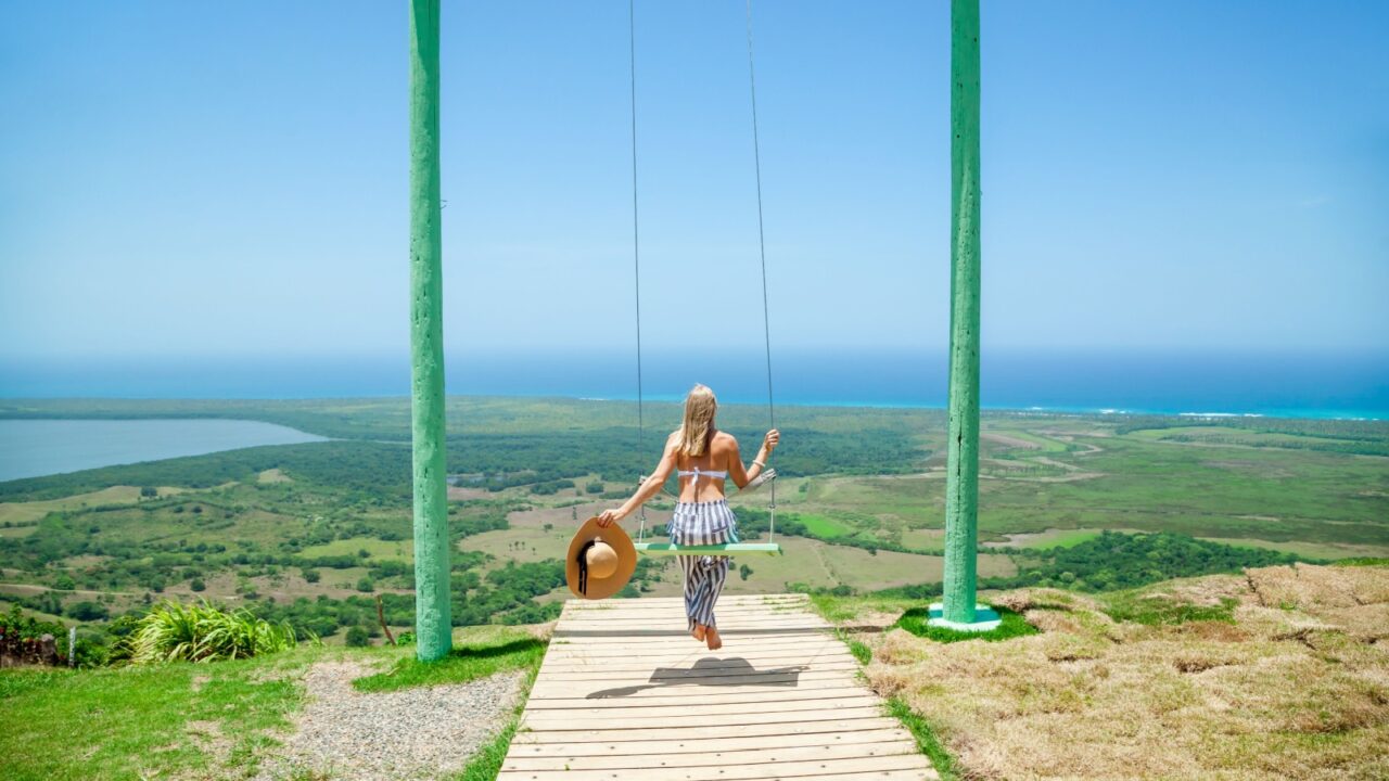 Woman swinging on swings over the green mountains with ocean sea caribbean tropical landscape and horizon line with blue sky. Montana Redonda, Dominican republic. Freedom concept.