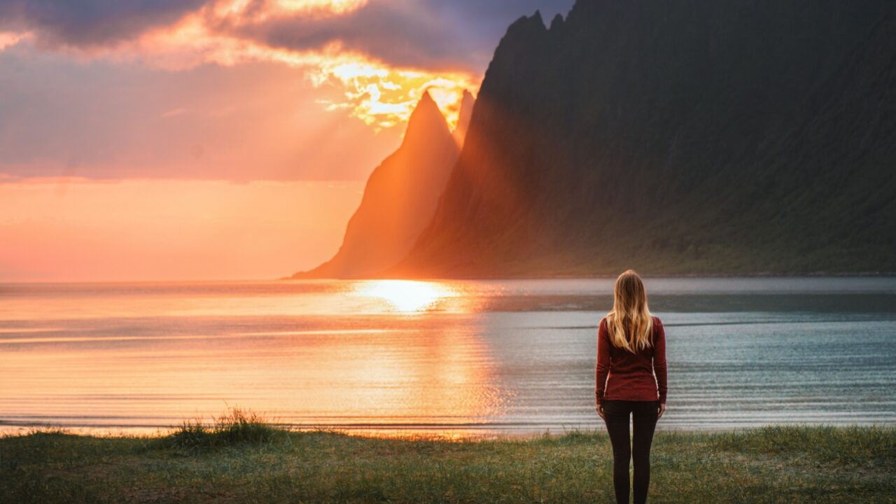 Woman traveling in Norway walking alone on sunset Ersfjord beach harmony with nature healthy lifestyle girl tourist enjoying Senja island midnight sun landscape sea and rocks summer vacations outdoor
