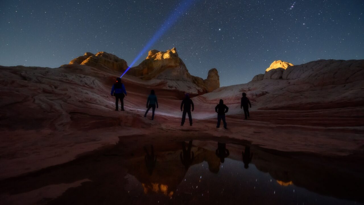 Group of stargazers posting under the night sky full of stars at White Pocket, remote area in Arizona desert. Inspring travel and adventure theme.