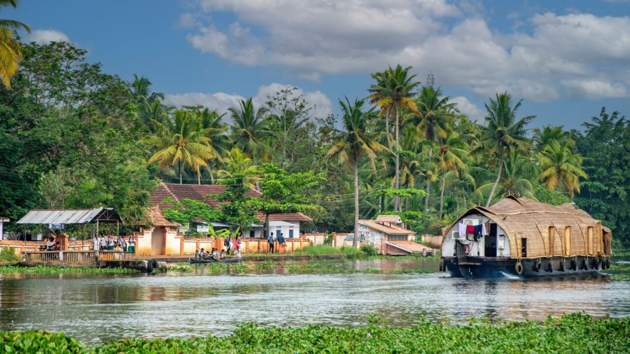 Alappuzha, Kerala, India - November 15, 2016: Traditional Keralan houseboat passing a village in the backwaters around Alappuzha (Alleppey).