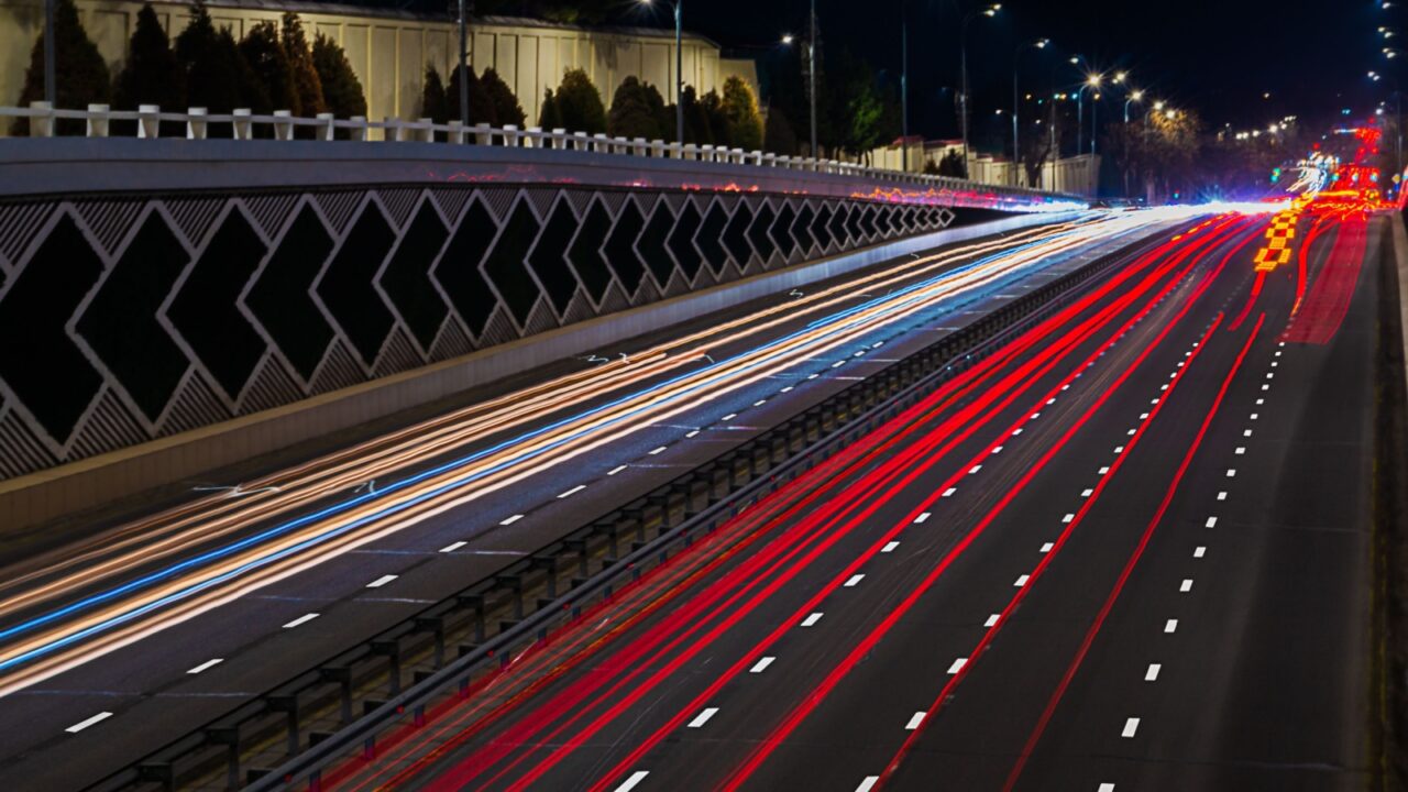 An eight-lane highway at night, illuminated by street lamps. The photo was taken with a long exposure, in which the movement of cars leaves light trails of yellow, blue, red.