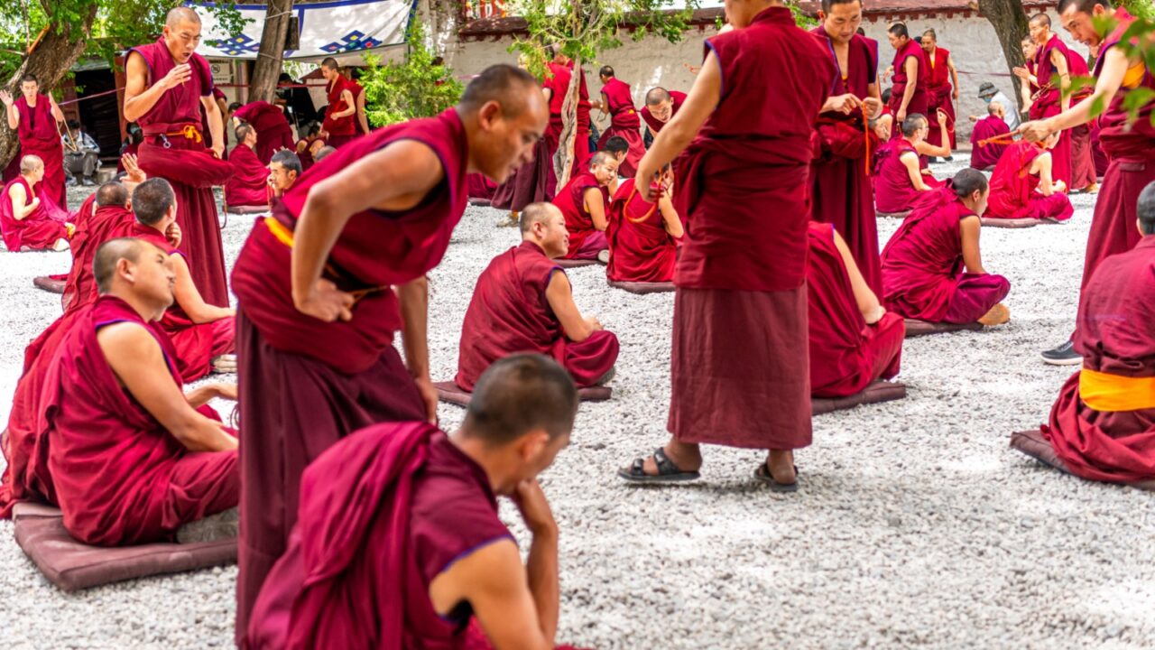 LHASA, TIBET, CHINA - JULY 5 2022: young monks practicing the art of debate in a sunny courtyard of Sera Monastery