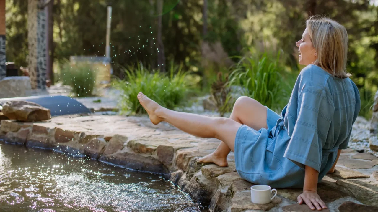 a happy young woman sitting by pond near cottege and
