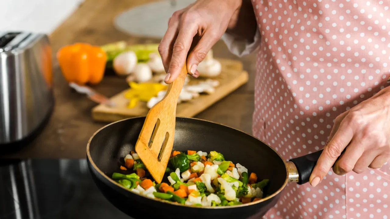 cropped image of mature woman frying vegetables in kitchen