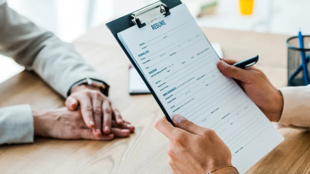 Cropped view of employee holding clipboard with resume letters near recruiter.