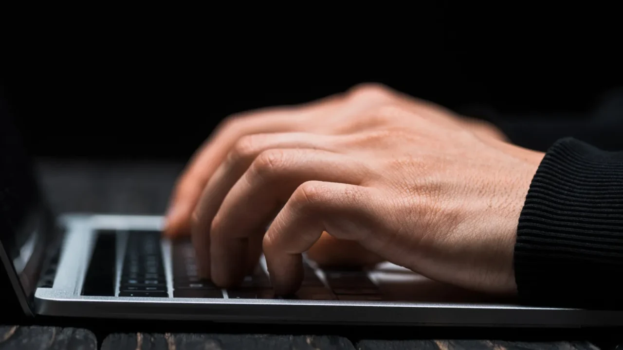 cropped view of hacker typing on laptop keyboard isolated on