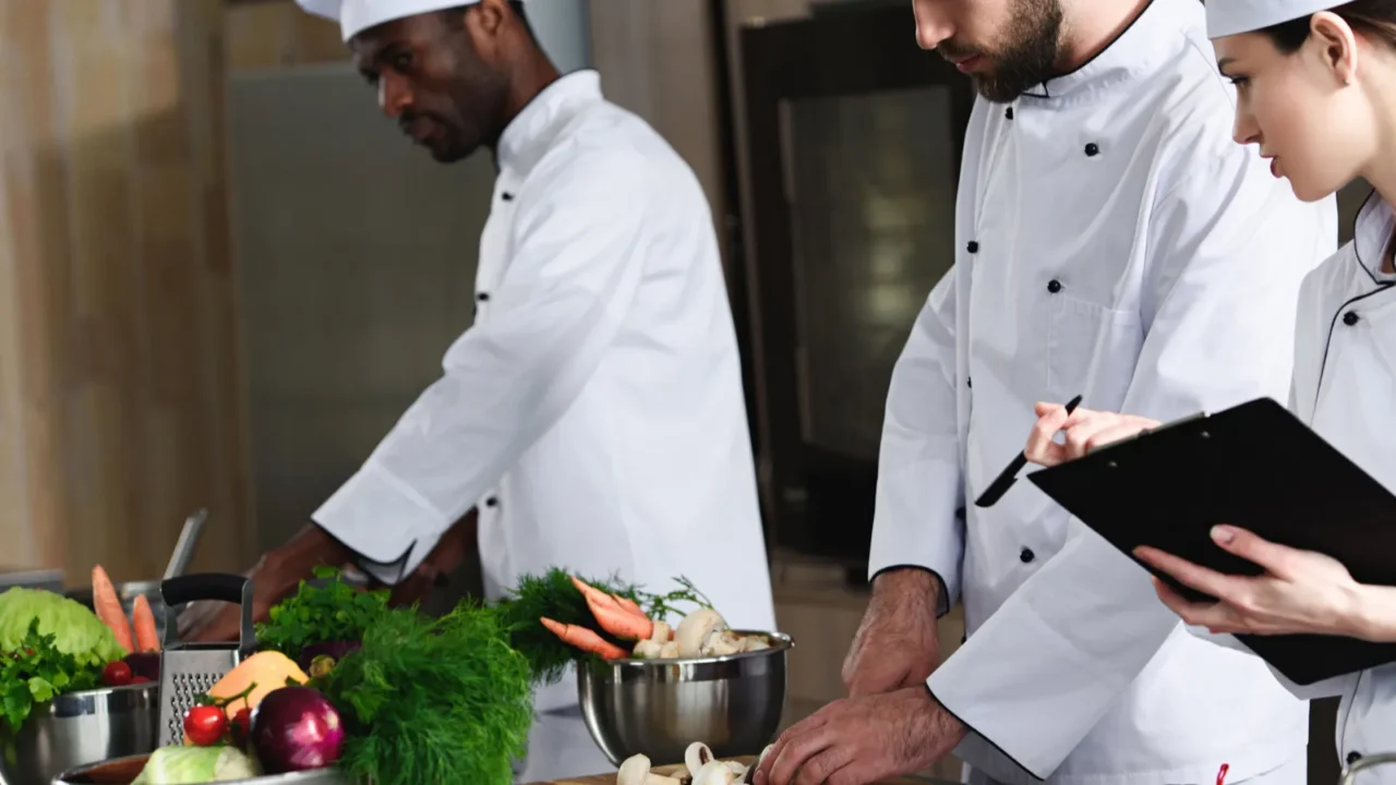 female chef writing down recipe by her multiracial colleagues