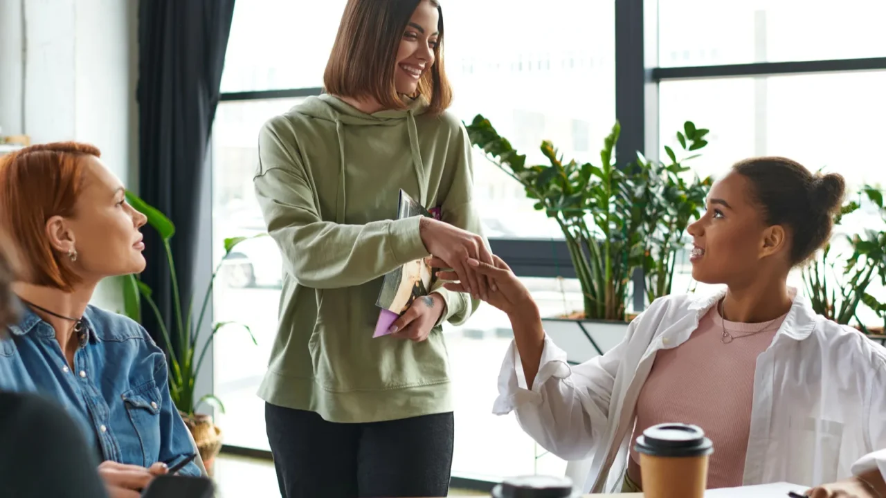 happy young woman holding magazines and shaking hands with african