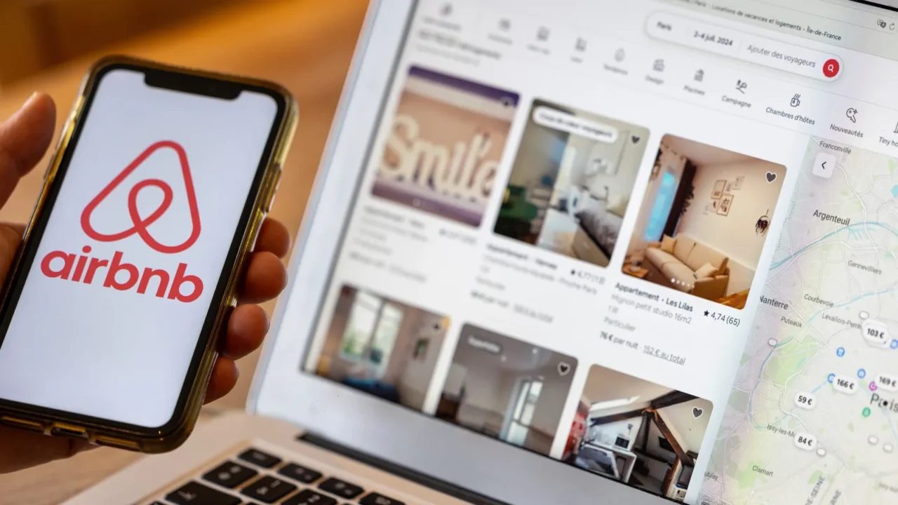 Female hand holding smartphone with Airbnb application, checking rental options in UK.