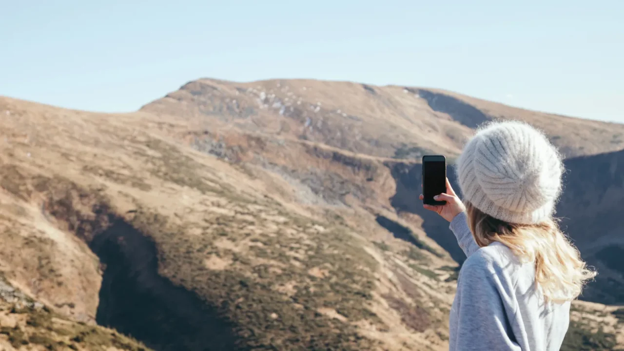 rear view of woman taking photo of mountain with smartphone