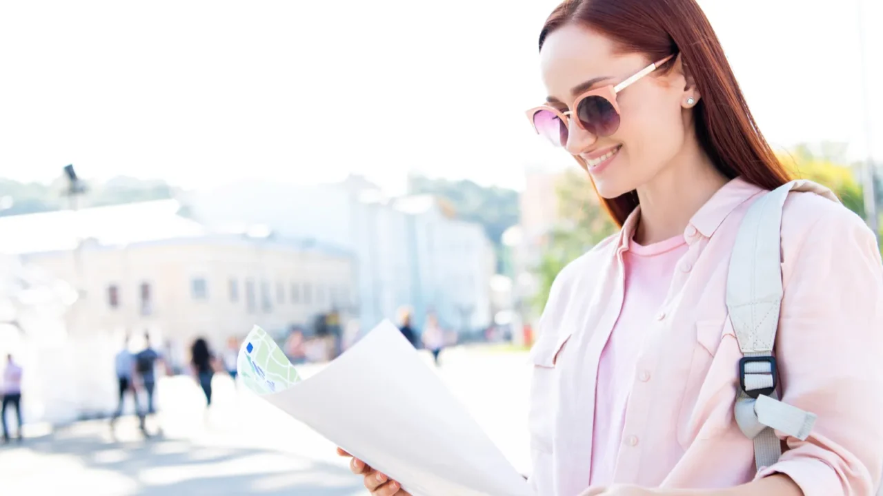 smiling attractive tourist in sunglasses looking at map on street