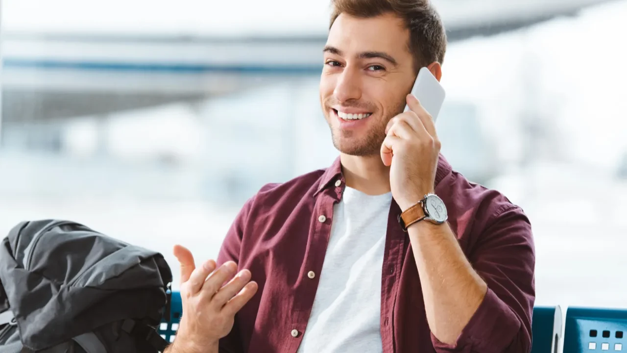 smiling man talking on smartphone while waiting in waiting hall