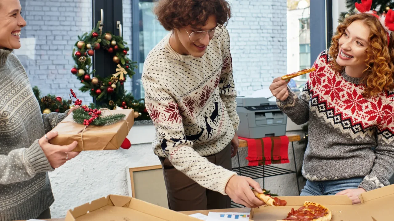 three coworkers share a festive moment enjoying pizza while exchanging