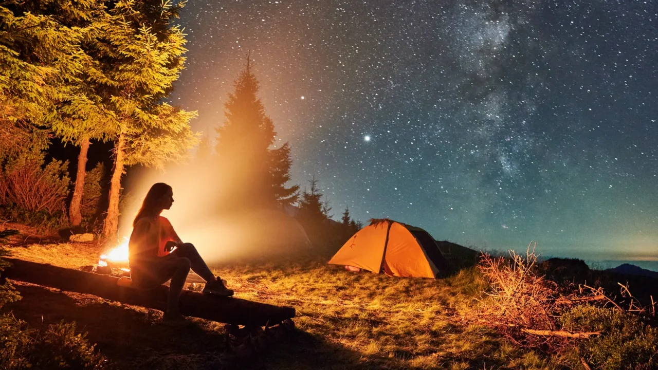 young woman hiker sitting on bench near bonfire under magical