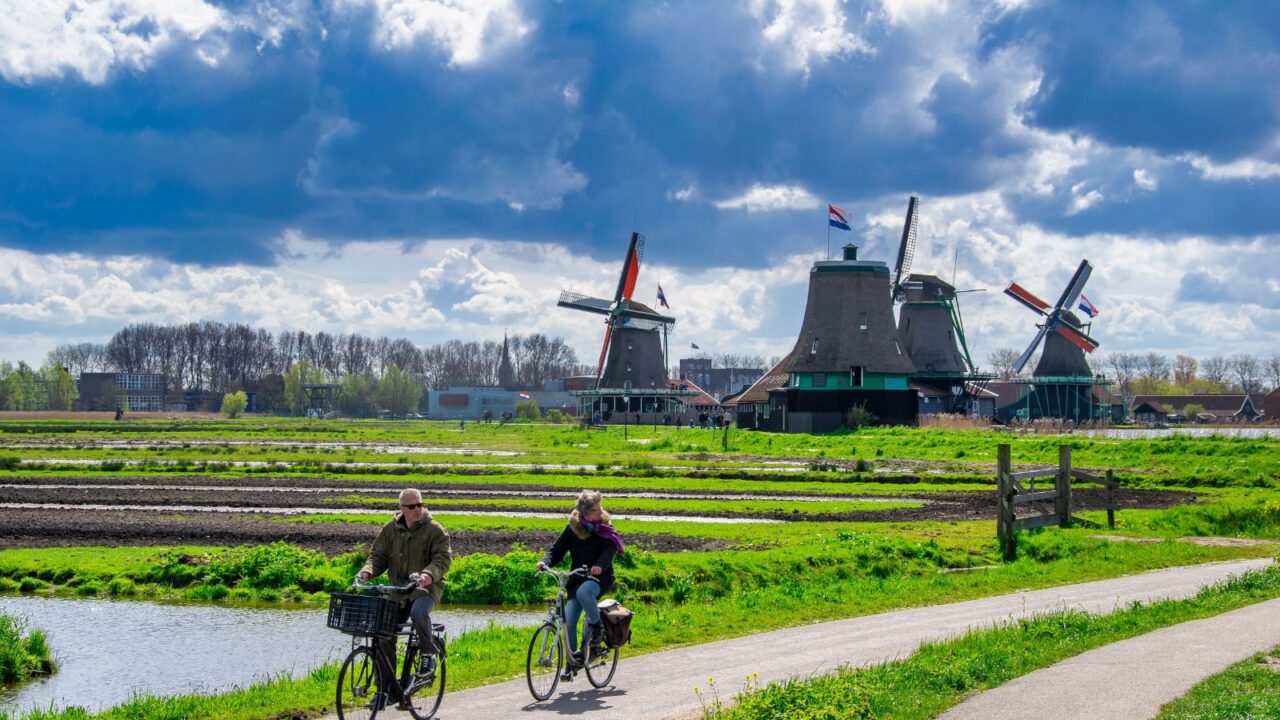 Famous windmills, warehouses and workshops on a sunny spring day with tourists riding bikes. ZAANSE SCHANS, THE NETHERLANDS.