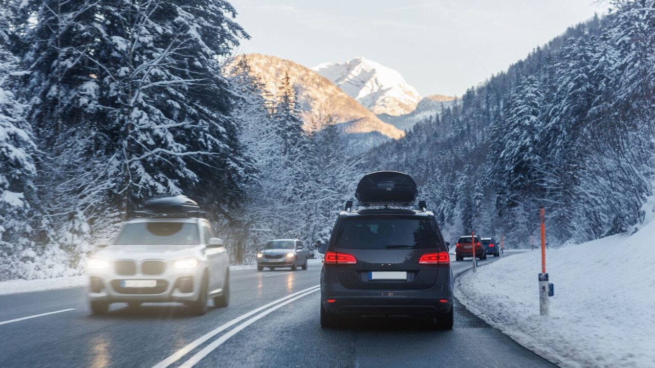 Scenic rear view of a family van with a roof box and luggage driving along an alpine countryside road on a cold winter day near a European mountain resort.